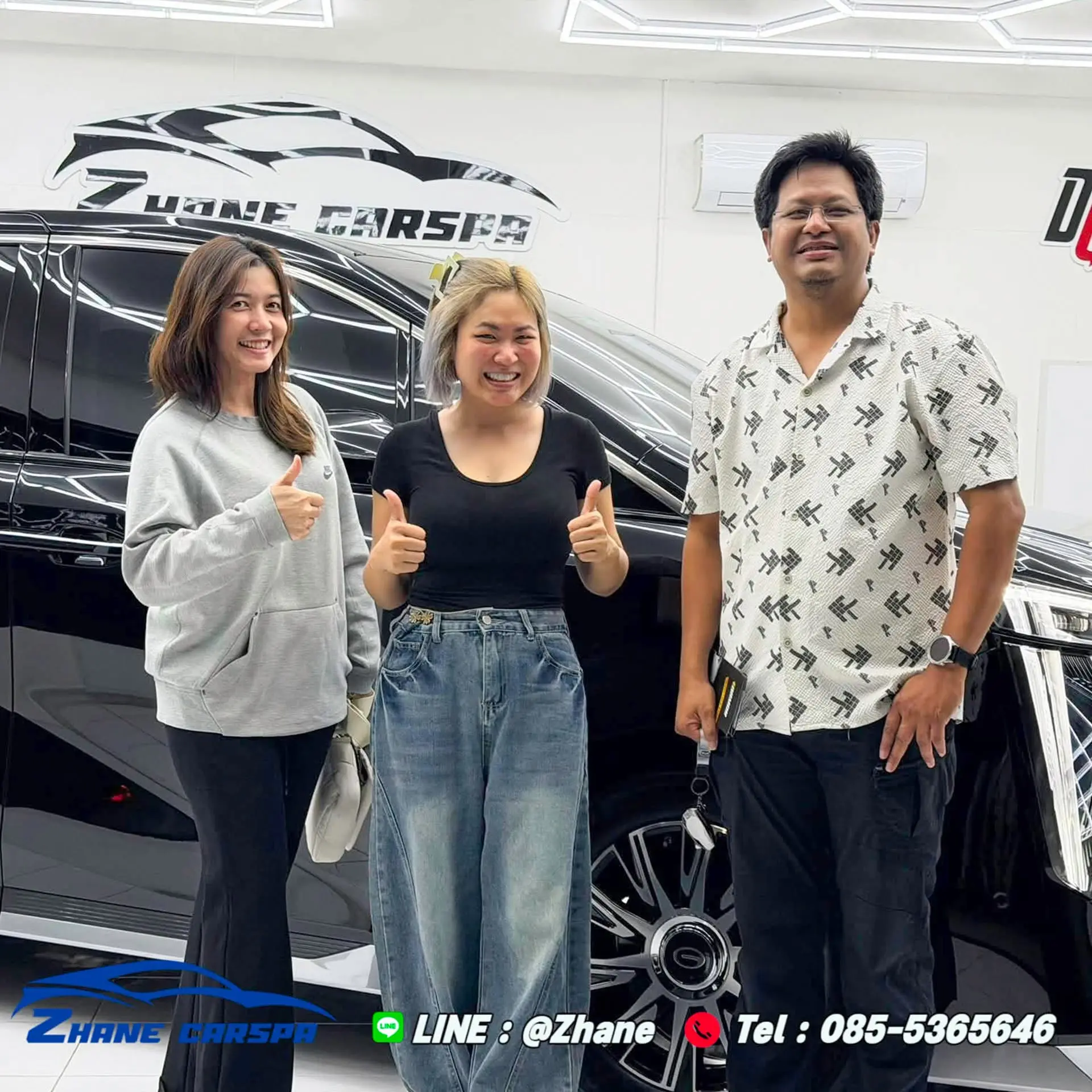 ลูกค้าสามคนยกนิ้วโป้งถ่ายรูปกับรถ GAC M8 สีดำหลังรับรถที่ติดฟิล์มกันรอยและเคลือบกราฟีน ในโชว์รูม Zhane Car Spa