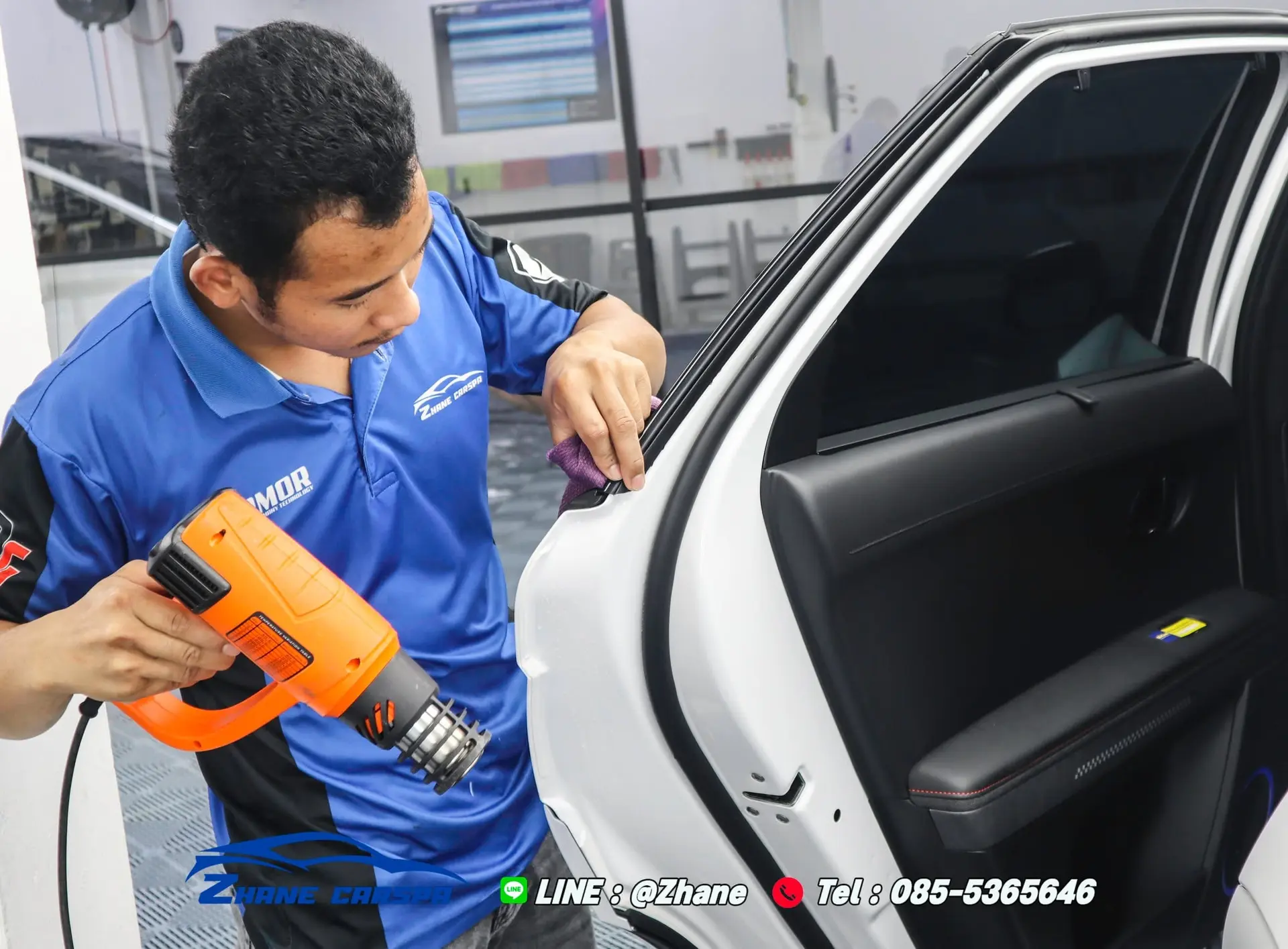 ช่าง Zhane Car Spa ใช้ปืนเป่าลมร้อนและผ้าไมโครไฟเบอร์เก็บขอบฟิล์มกันรอยที่ขอบประตูหลังรถสีขาว