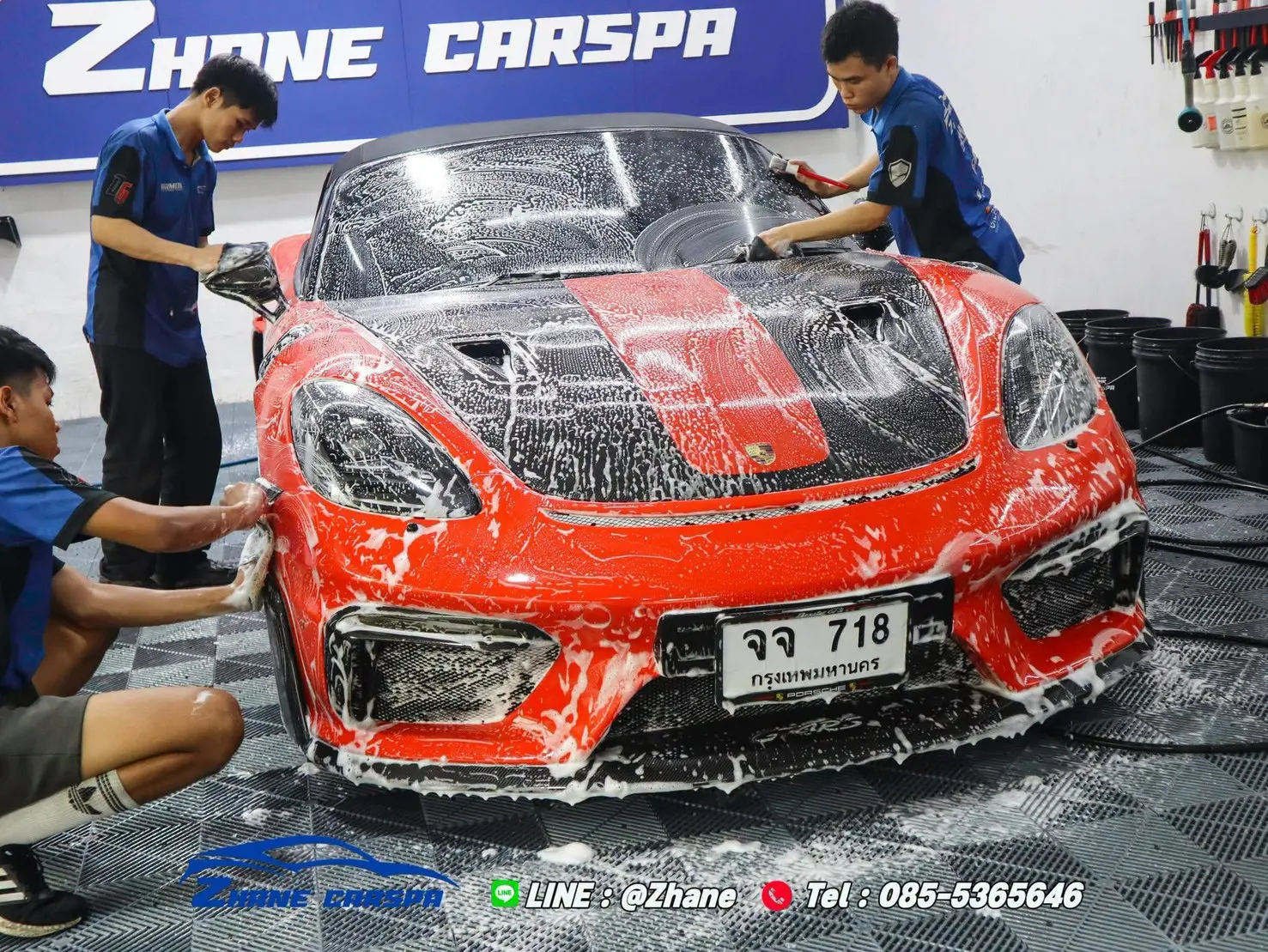 ช่างสามคนล้างรถ Porsche 718 สีแดงคาดดำด้วยโฟมและถุงมือล้างรถ ทั้งกระจกหน้า ฝากระโปรง และกันชนหน้า