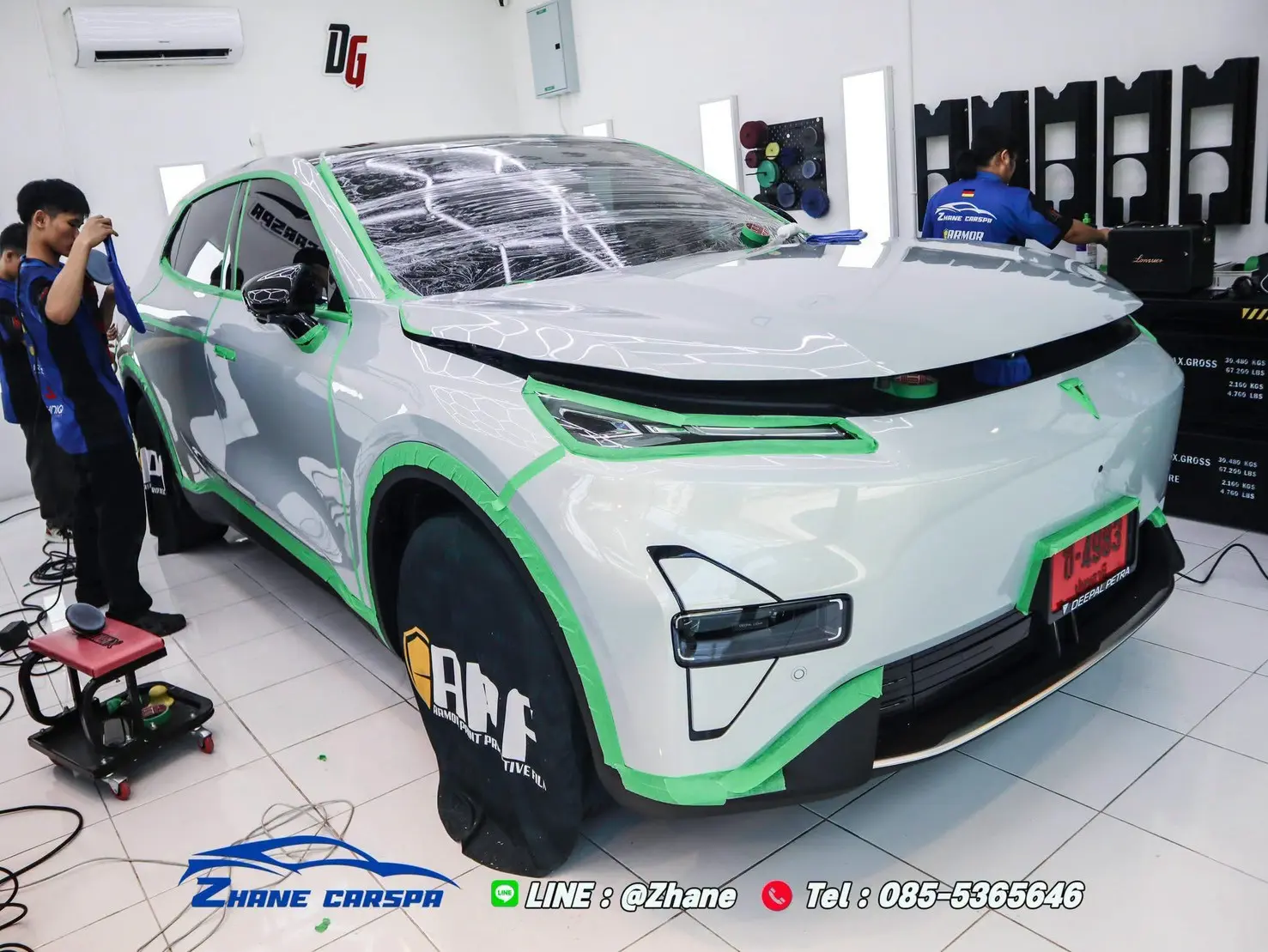 รถ SUV ไฟฟ้าสีเทาเงินติดเทปสีเขียวรอบไฟหน้า ซุ้มล้อ และกันชน พร้อมฟิล์มคลุมกระจกหน้าและผ้าคลุมล้อ