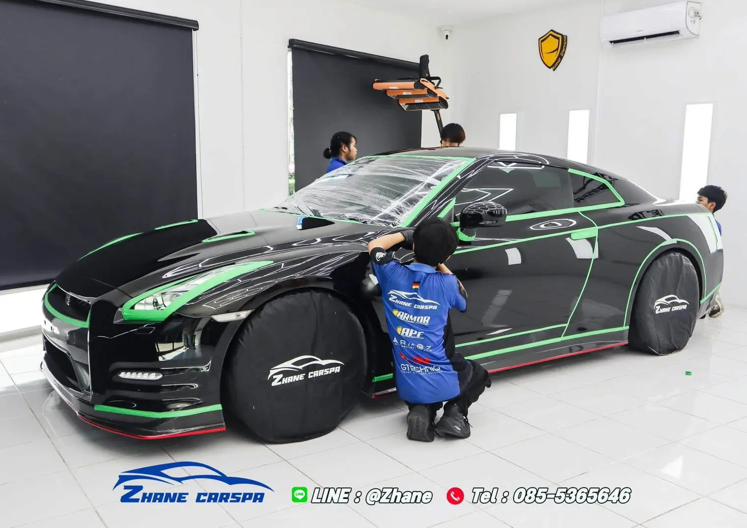 ทีมช่างติดเทปสีเขียวตามขอบกระจก ขอบประตู ไฟหน้า และชายล่างรถ Nissan GT-R R35 สีดำ พร้อมผ้าคลุมล้อ ก่อนเริ่มขัดสี