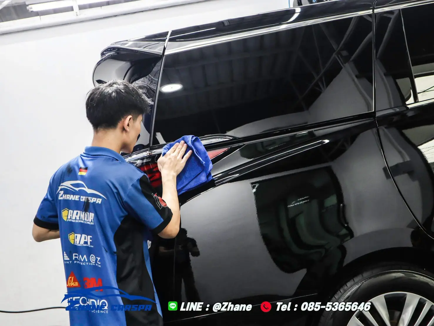 ช่างใช้ผ้าไมโครไฟเบอร์สีฟ้าเช็ดผิวสีบริเวณไฟท้ายรถ Toyota Alphard สีดำ