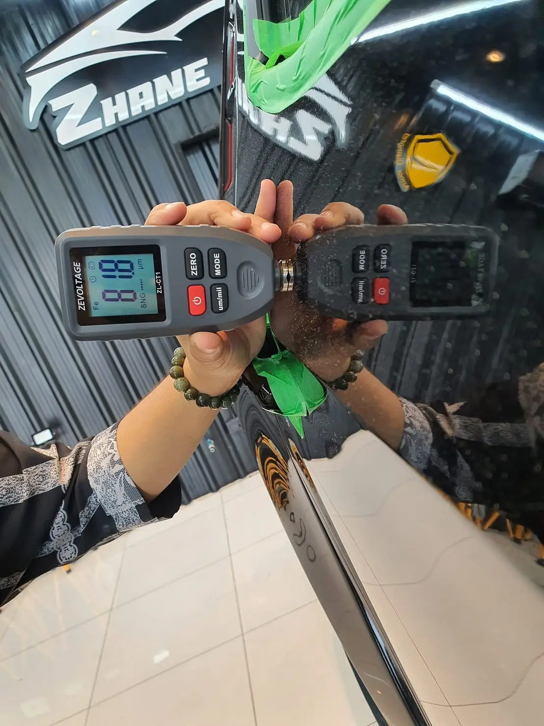 ช่างวัดความหนาชั้นสีบนประตูรถสีดำเงาด้วยเครื่อง paint gauge เห็นเงาสะท้อนของเครื่องบนผิวสี
