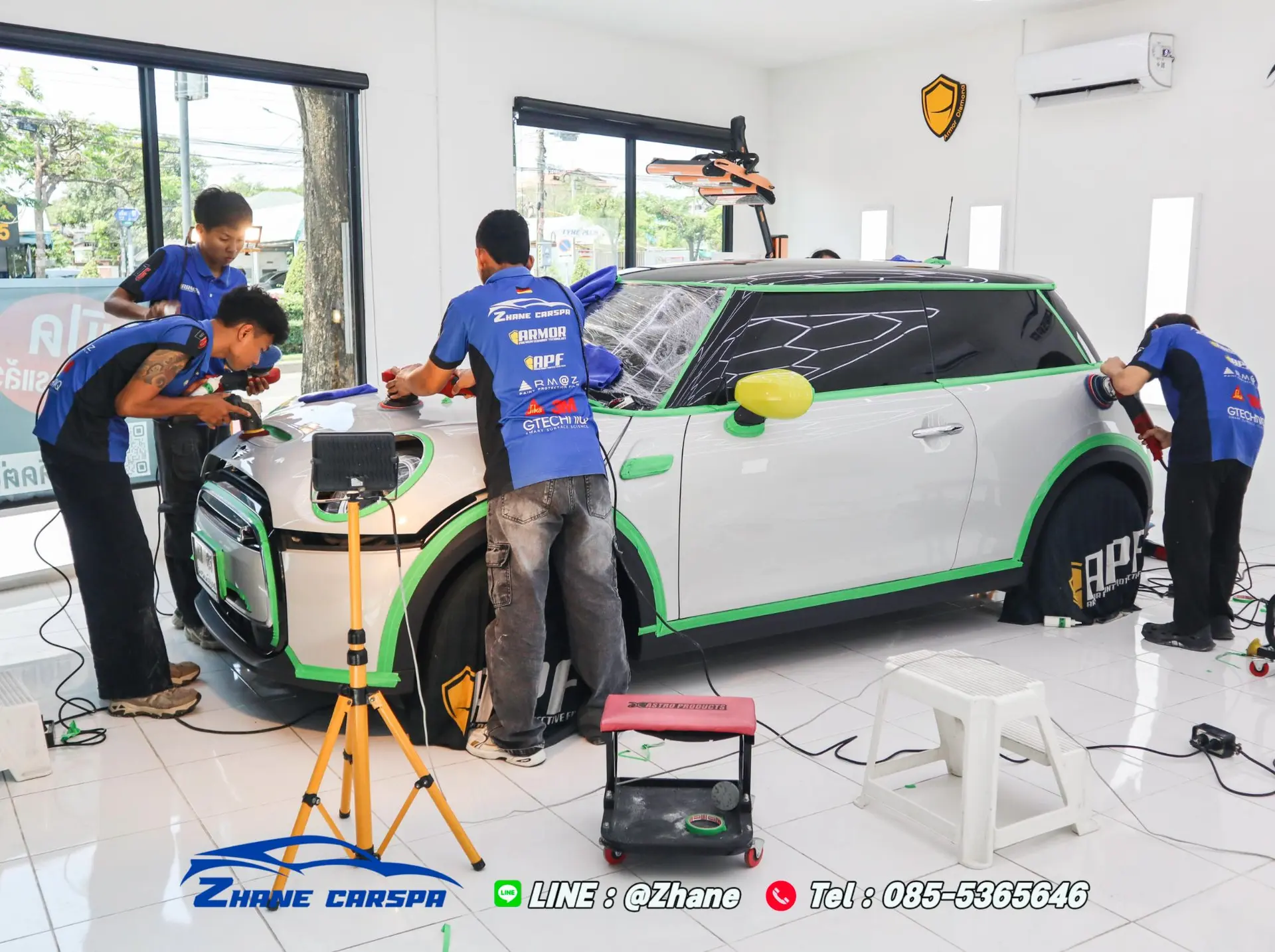 ช่าง Zhane Carspa 4 คนใช้เครื่องขัด DA ขัดลบรอยรอบคัน MINI Cooper SE สีเงินที่ติดเทปสีเขียวป้องกันขอบยางและพลาสติกก่อนเคลือบเซรามิก