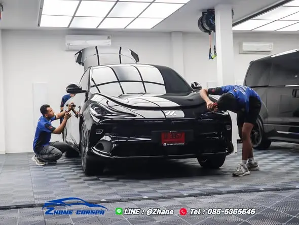 ช่าง Zhane Car Spa สองคนกำลังติดฟิล์มใสกันรอย PPF บริเวณหน้ารถ MG IM6 รถยนต์ไฟฟ้าในร้าน