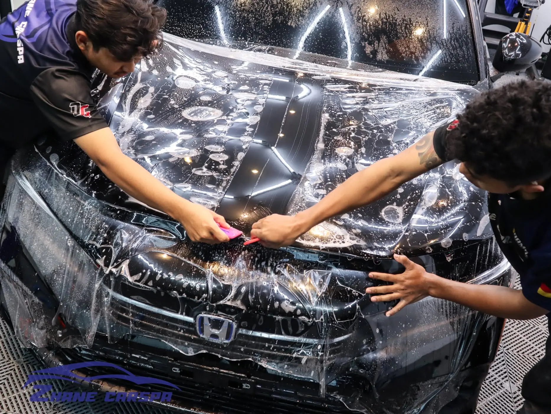 ช่าง Zhane Car Spa สองคนกำลังติดฟิล์มใสกันรอยบนฝากระโปรงหน้า Honda Civic สีดำป้ายแดง
