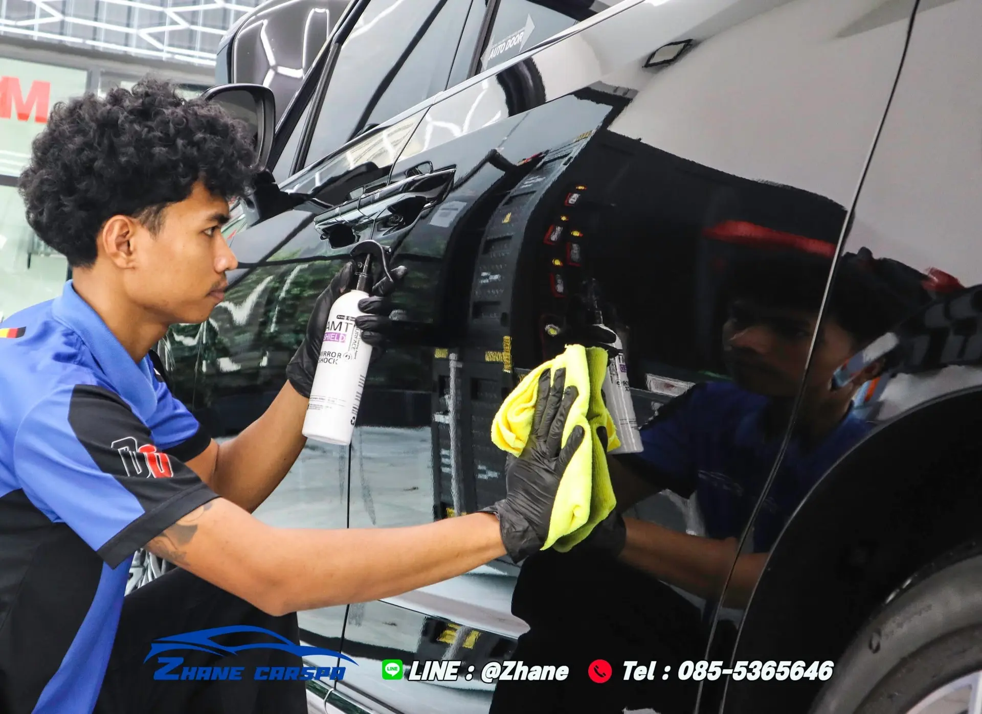 ช่าง Zhane Car Spa สวมถุงมือดำฉีดสเปรย์น้ำยาดูแลฟิล์มและเช็ดประตู MG Maxus 9 สีดำด้วยผ้าไมโครไฟเบอร์สีเหลือง ระหว่างเซอร์วิสรอบ 6 เดือน