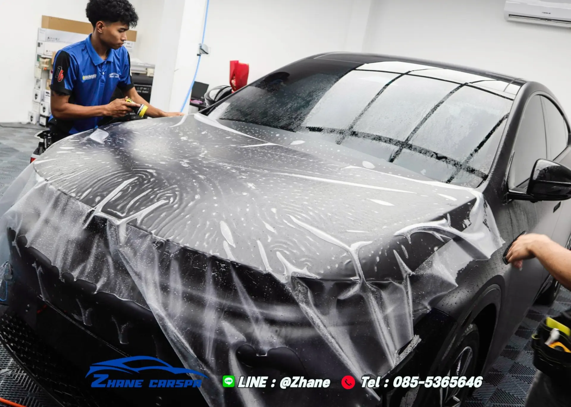 ช่าง Zhane Car Spa กำลังวางแผ่นฟิล์มใสกันรอยเต็มแผ่นคลุมฝากระโปรงรถเก๋งสีดำ